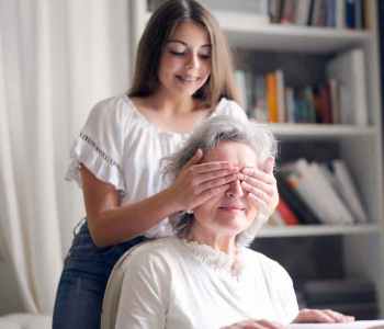 cheerful teenager playing with grandmother guess who game while making surprise in light living room